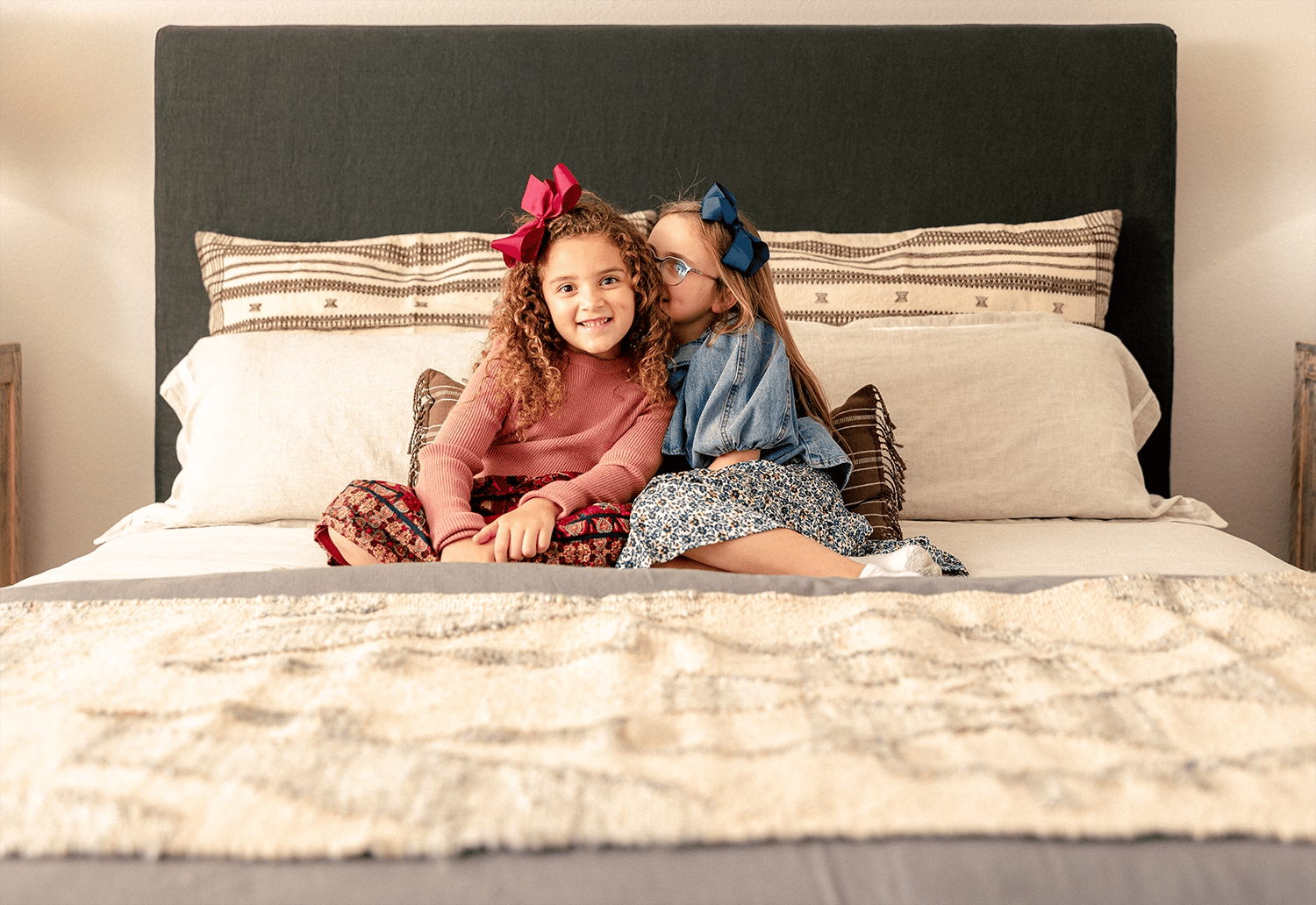 Photo of two sisters whispering secrets to each other while sitting on a bed in their Betenbough home.