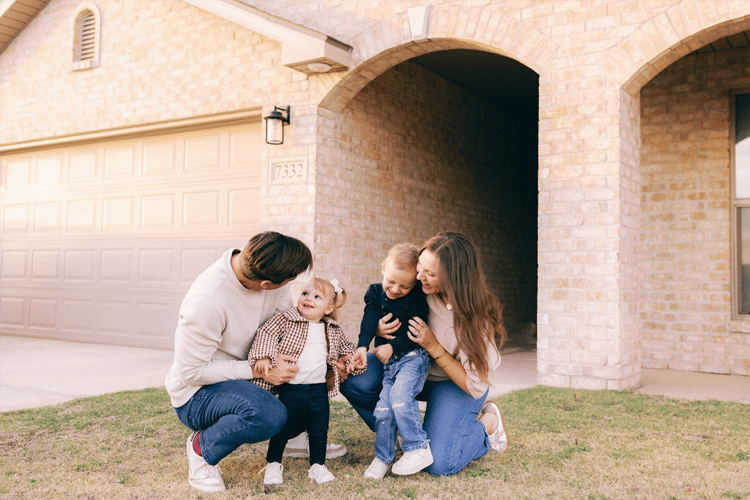 Photo of a family with their young son and daughter interacting on the front lawn in front of their Betenbough home. Betenbough Homes builds new homes in Lubbock Tx.