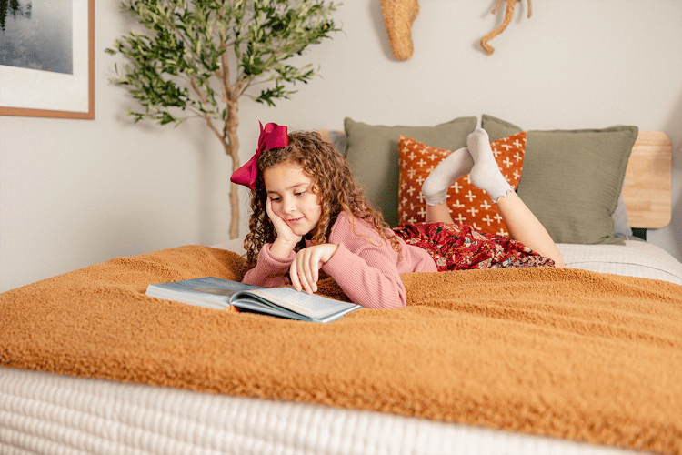 Photo of a young girl reading on her bed in a Betenbough home. Betenbough Homes builds new homes in Lubbock Tx.
